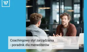 Dwóch mężczyzn rozmawia przy biurku. Jeden z nich, w brązowej koszuli, gestykuluje, wyjaśniając coś. Widać, że stosuje coachingowy styl zarządzania, wspierając pracownika.
