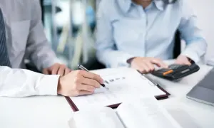 Analiza mocne i słabe strony lidera. Dwie osoby przy biurku, jedna pisze, druga liczy na kalkulatorze.