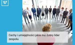 Grupa ludzi w garniturach stoi w kręgu, słuchając swojego **team leadera**.
